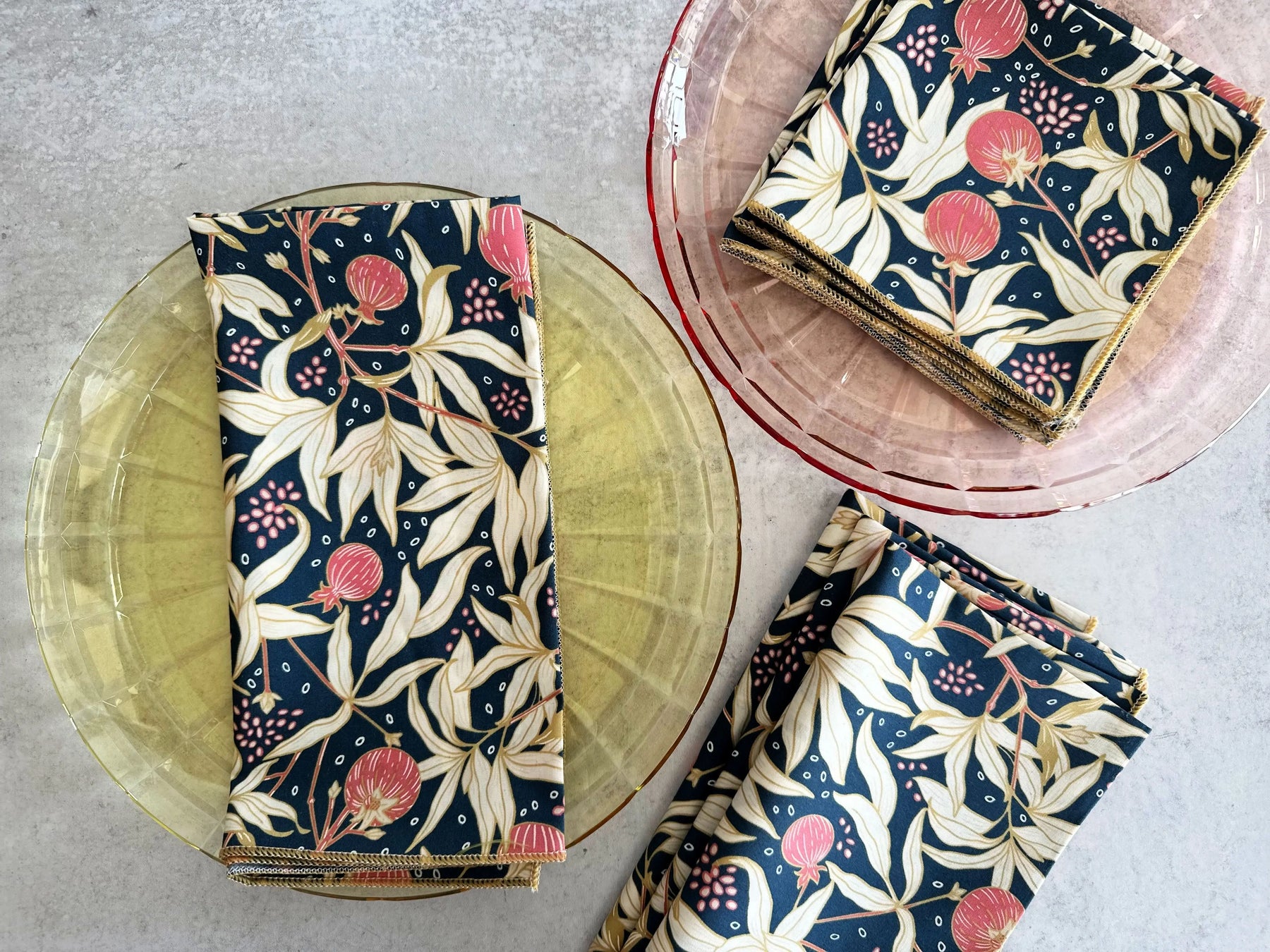 Four navy blue cloth napkins with a floral pattern featuring pink fruits and cream leaves.