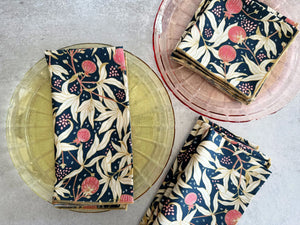 Four navy blue cloth napkins with a floral pattern featuring pink fruits and cream leaves.