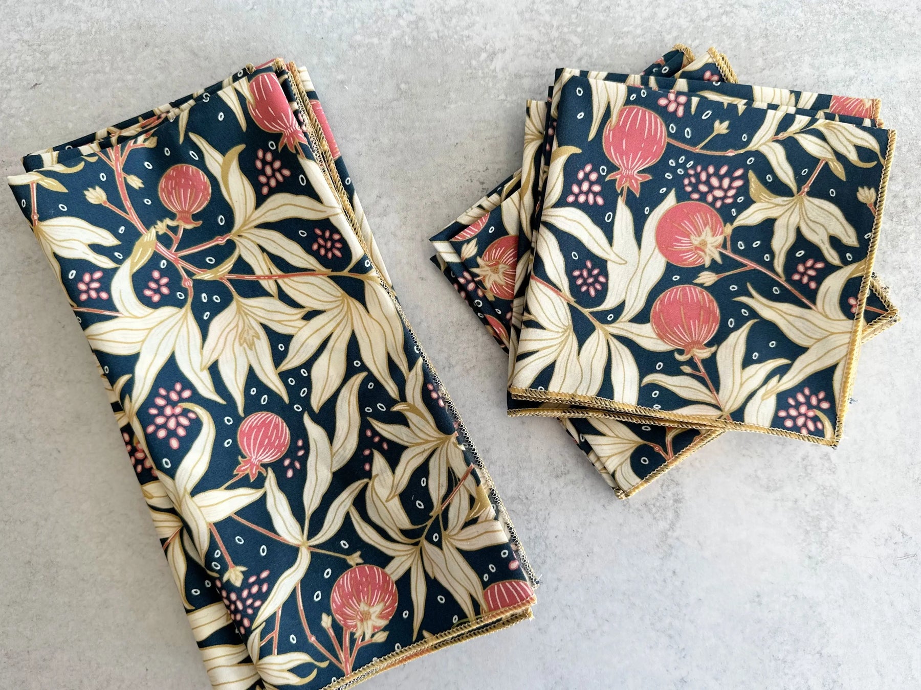 Dark blue cloth napkins with gold trim featuring pomegranate and leaf pattern.
