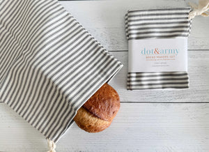 Two striped fabric bread bags with one loaf of bread and product packaging.