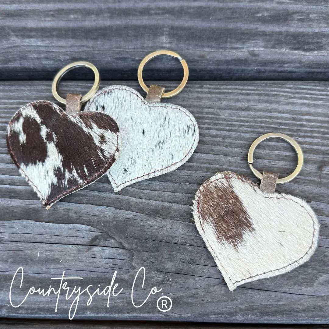 Heart-shaped cowhide keychain with brown and white patches.