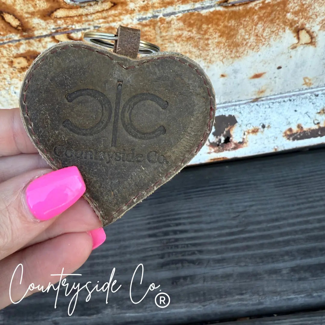 Heart-shaped cowhide keychain with 'Countryside Co.' branding.