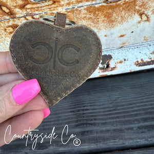 Heart-shaped cowhide keychain with 'Countryside Co.' branding.