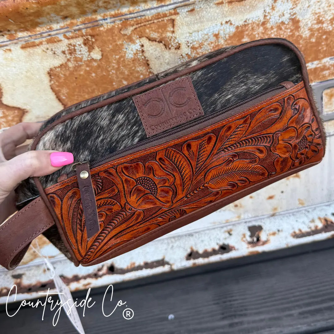 Brown tooled leather and cowhide toiletry bag with floral pattern and zipper closure.