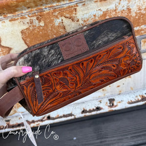 Brown tooled leather and cowhide toiletry bag with floral pattern and zipper closure.