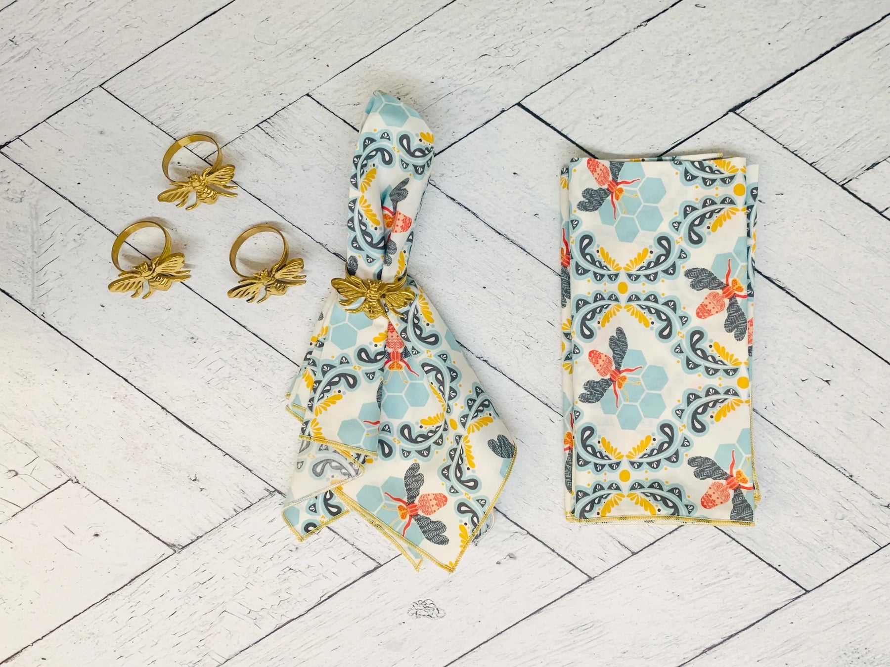Cotton honey bee cloth napkins and gold bee napkin rings on white wood background.