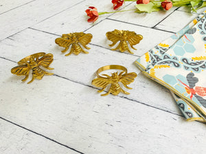 Gold bee napkin rings and folded cotton cloth napkins with pattern on white surface.