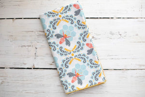 White cloth napkins with a repeating pattern of bees, hexagons, and floral designs in blue, orange, and gray.