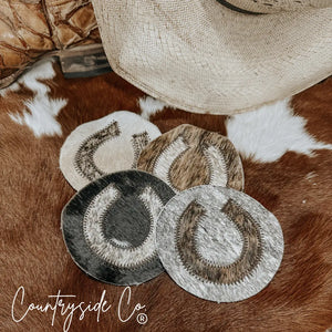 Set of 4 cowhide horseshoe coasters on a brown and white spotted hide.