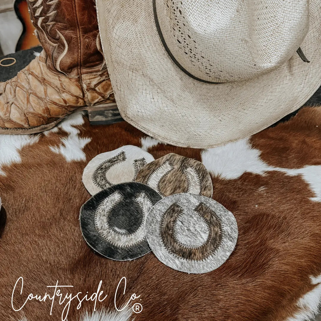 Set of four horseshoe cowhide coasters on a cowhide rug.