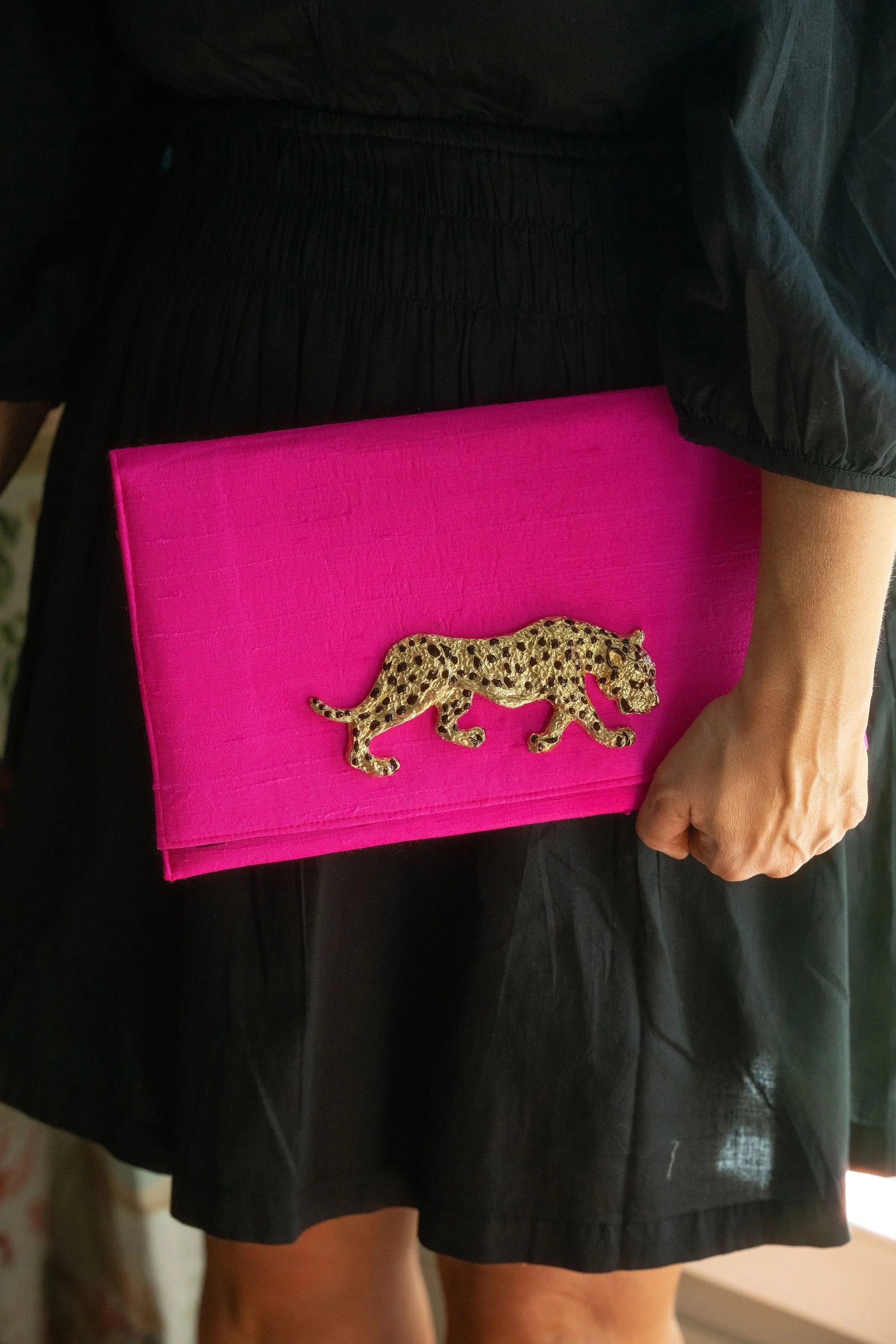 Hot pink clutch with gold leopard design held by a person.