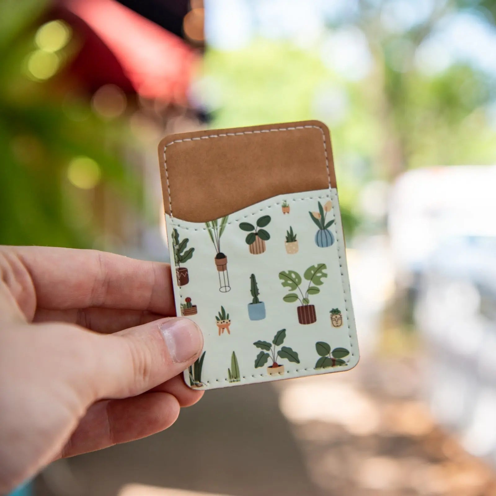 Adhesive phone wallet with a houseplant pattern held in a hand