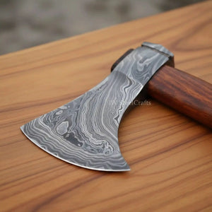 Damascus steel axe head with wood handle on rustic wood surface