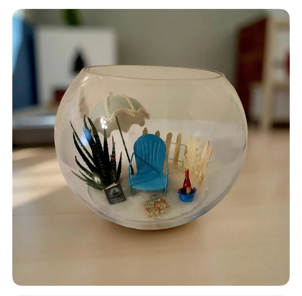Island beach scene in glass bowl with chair, umbrella, and sand. Decorative tabletop centerpiece.