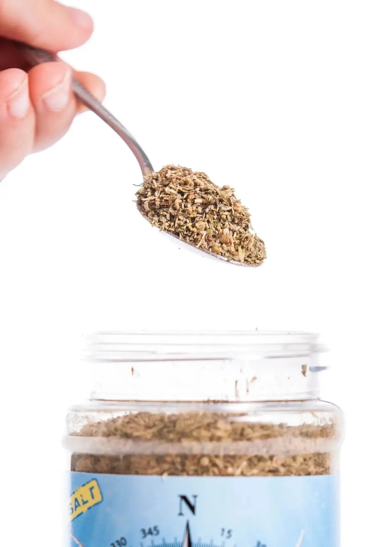 Italian Seasoning: Spoonful of herbs being poured into jar. Delicious seasoning for cooking!