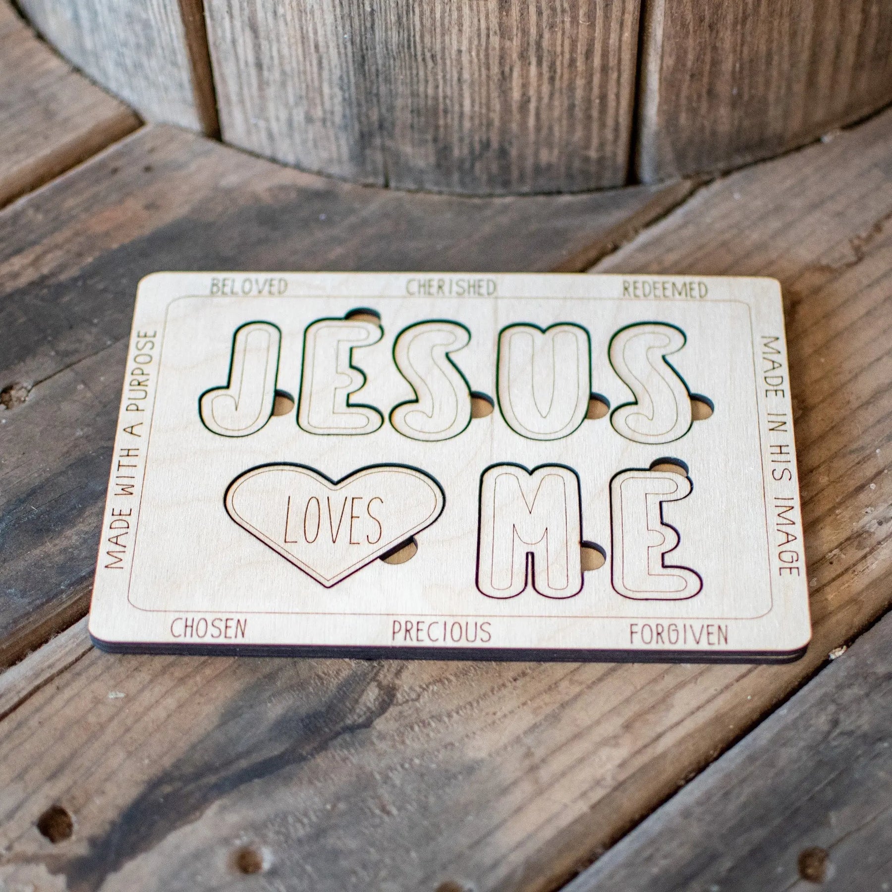 Wooden 'Jesus Loves Me' cutout puzzle with encouraging words on a wood surface.