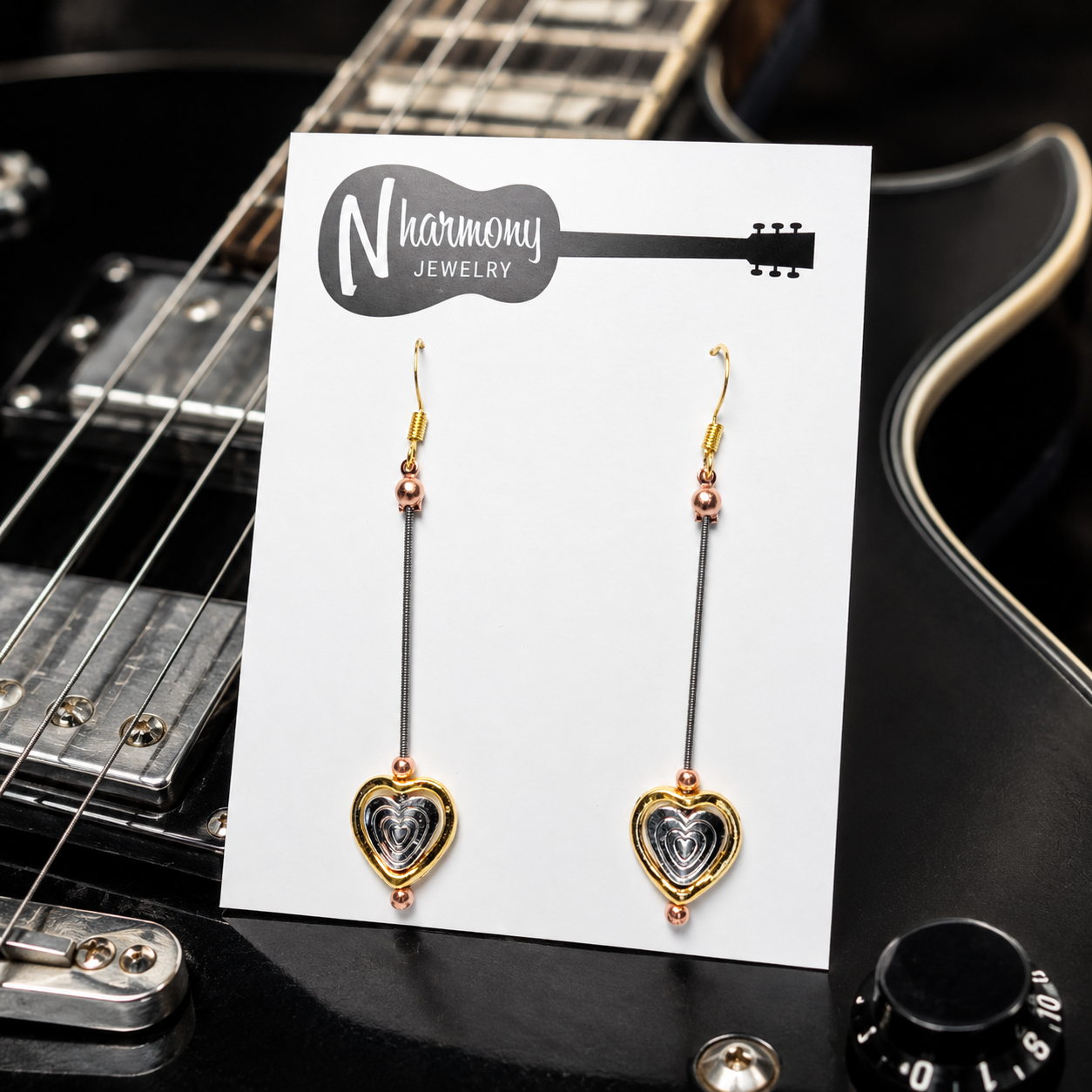 Heart-shaped earrings on a 'N Harmony Jewelry' card with a guitar in the background