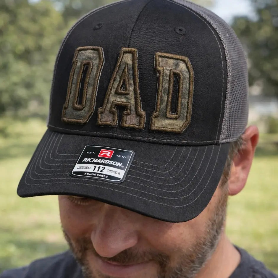 Black trucker hat with "DAD" embroidered in camouflage letters and Richardson brand tag.