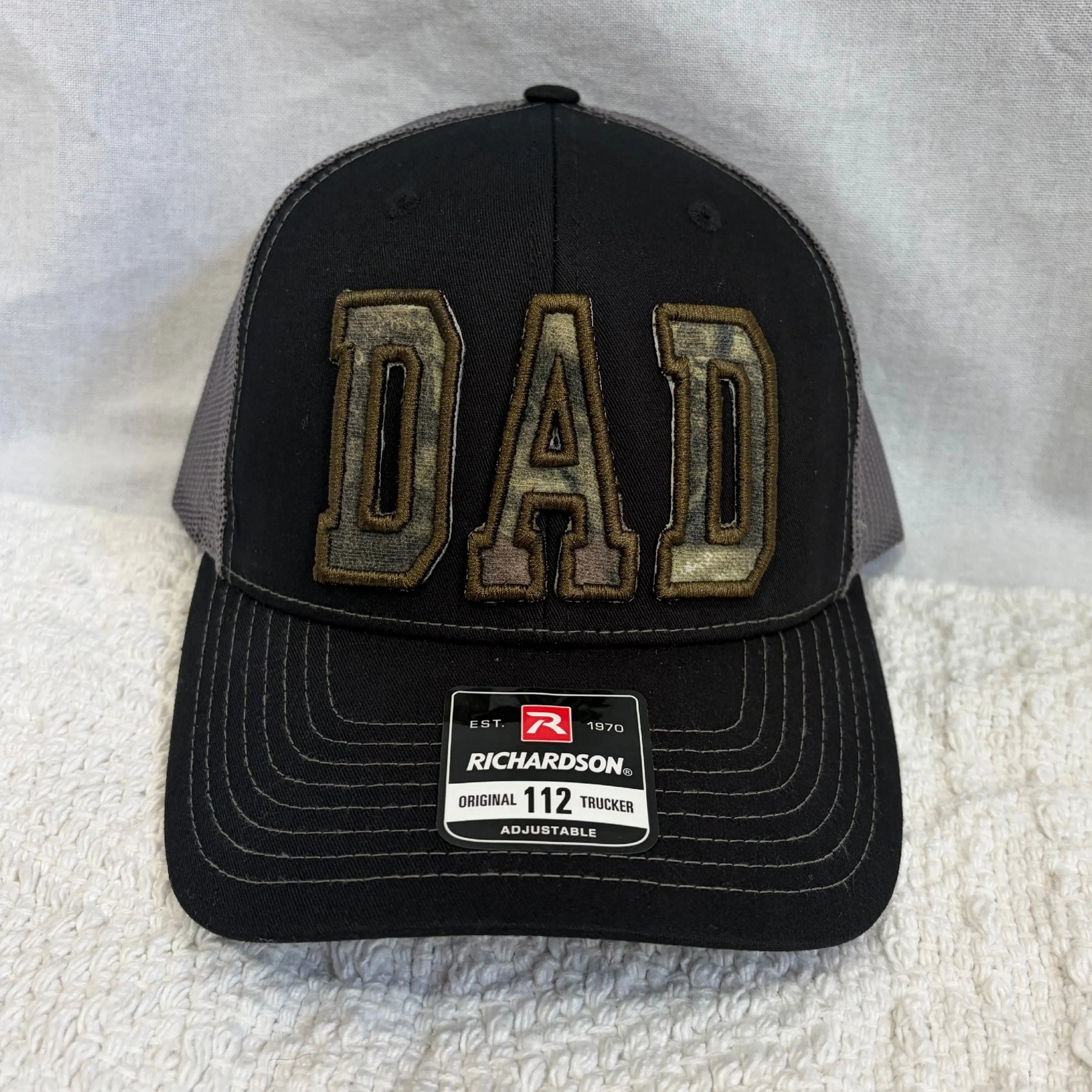 Black trucker hat with custom camouflage "DAD" appliqué and Richardson tag.