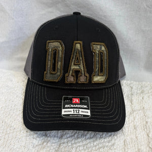 Black trucker hat with custom camouflage "DAD" appliqué and Richardson tag.