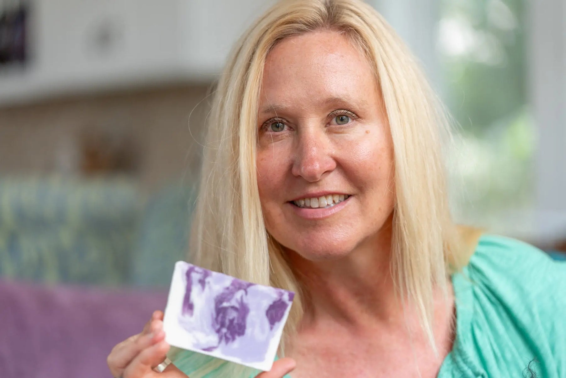 Woman holding a bar of lavender goat's milk soap with purple swirls.