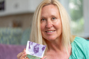 Woman holding a bar of lavender goat's milk soap with purple swirls.