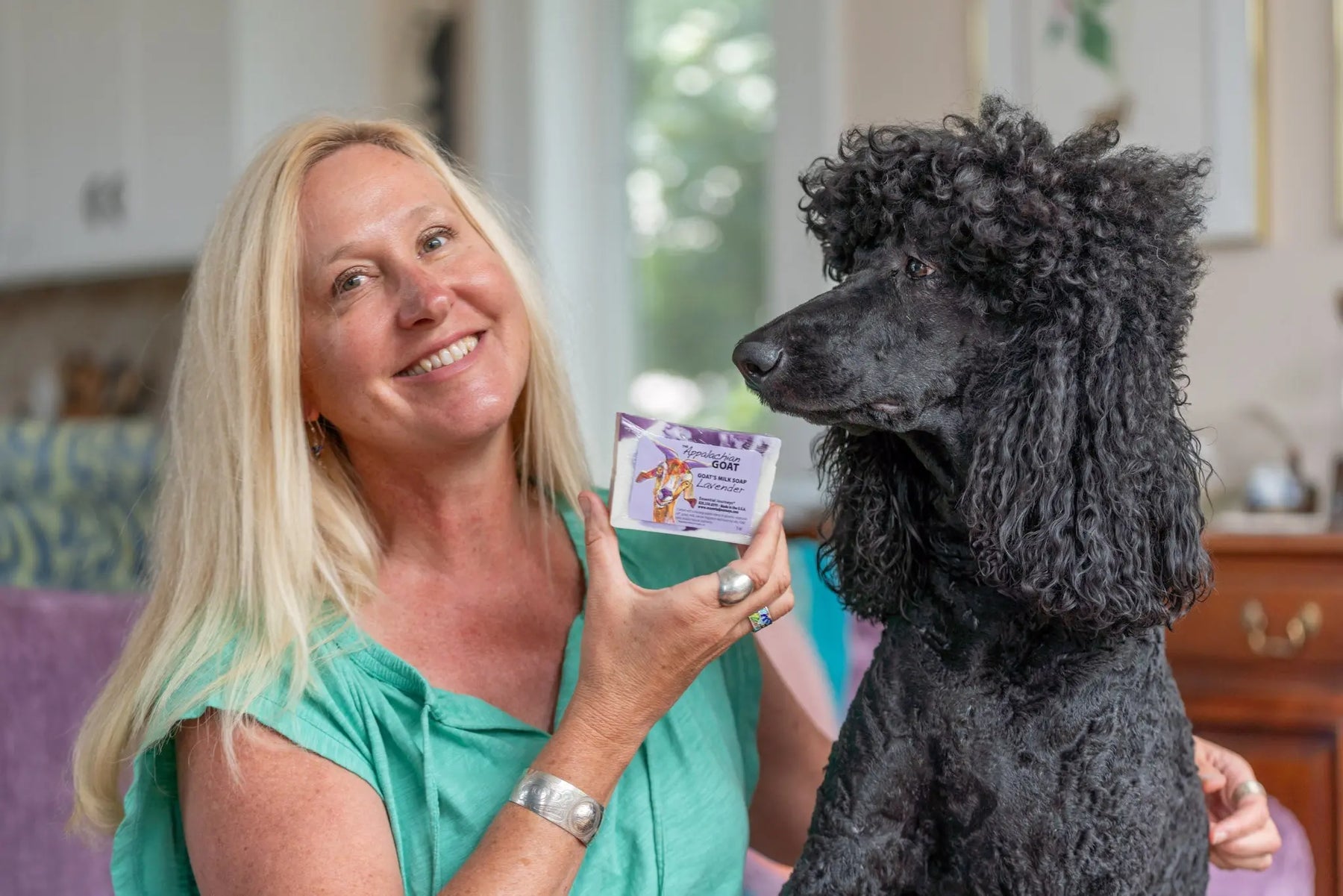 Black poodle with woman holding lavender goat milk soap slice