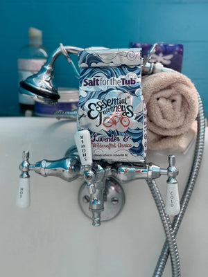 Essential Journeys Lavender & Arnica bath salts packaging in a bathtub.