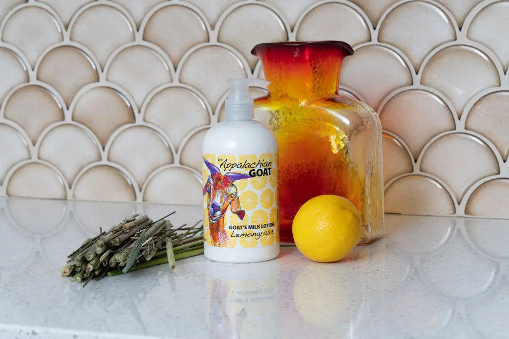 Goat's milk lotion bottle with lemongrass scent label, a lemon, and dried herbs.