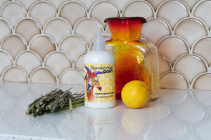 Goat's milk lotion bottle with lemongrass scent label, a lemon, and dried herbs.