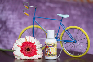 Bottle of lemongrass goat's milk lotion with a miniature bicycle and a gerbera daisy.