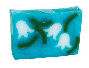 Blue soap slice with embedded white lily of the valley flowers and green stems.