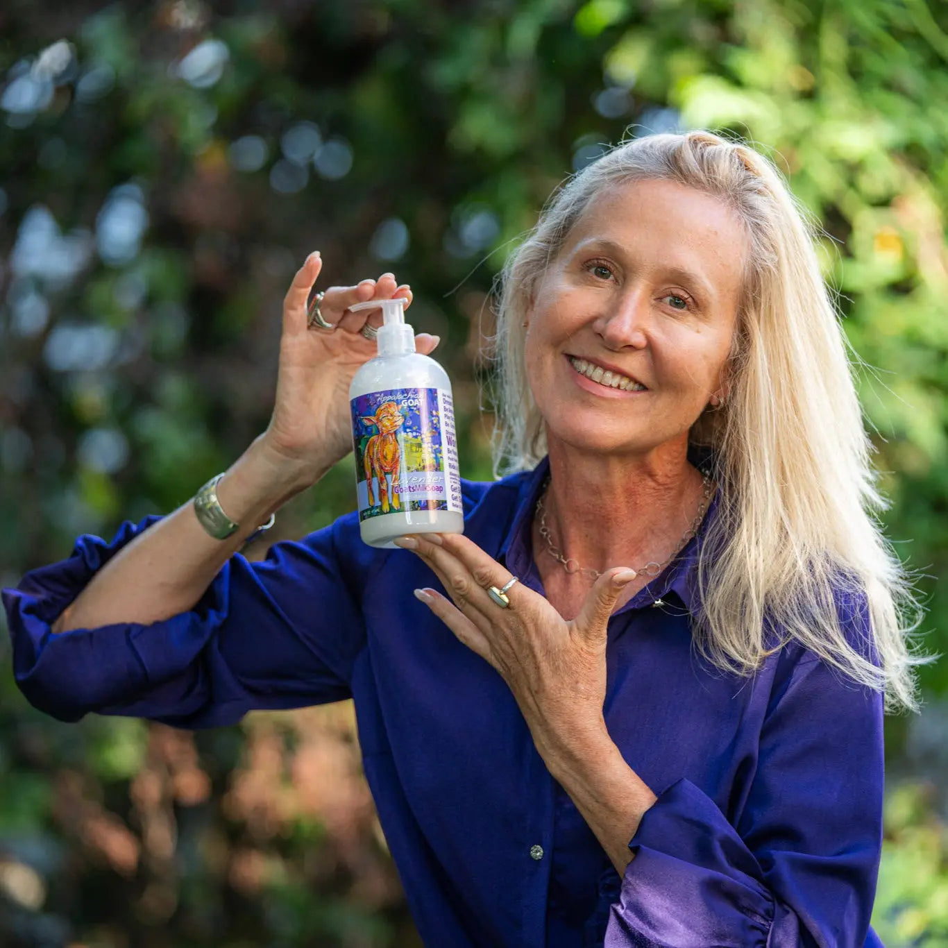 Woman holding a bottle of lavender goats milk liquid soap outdoors.