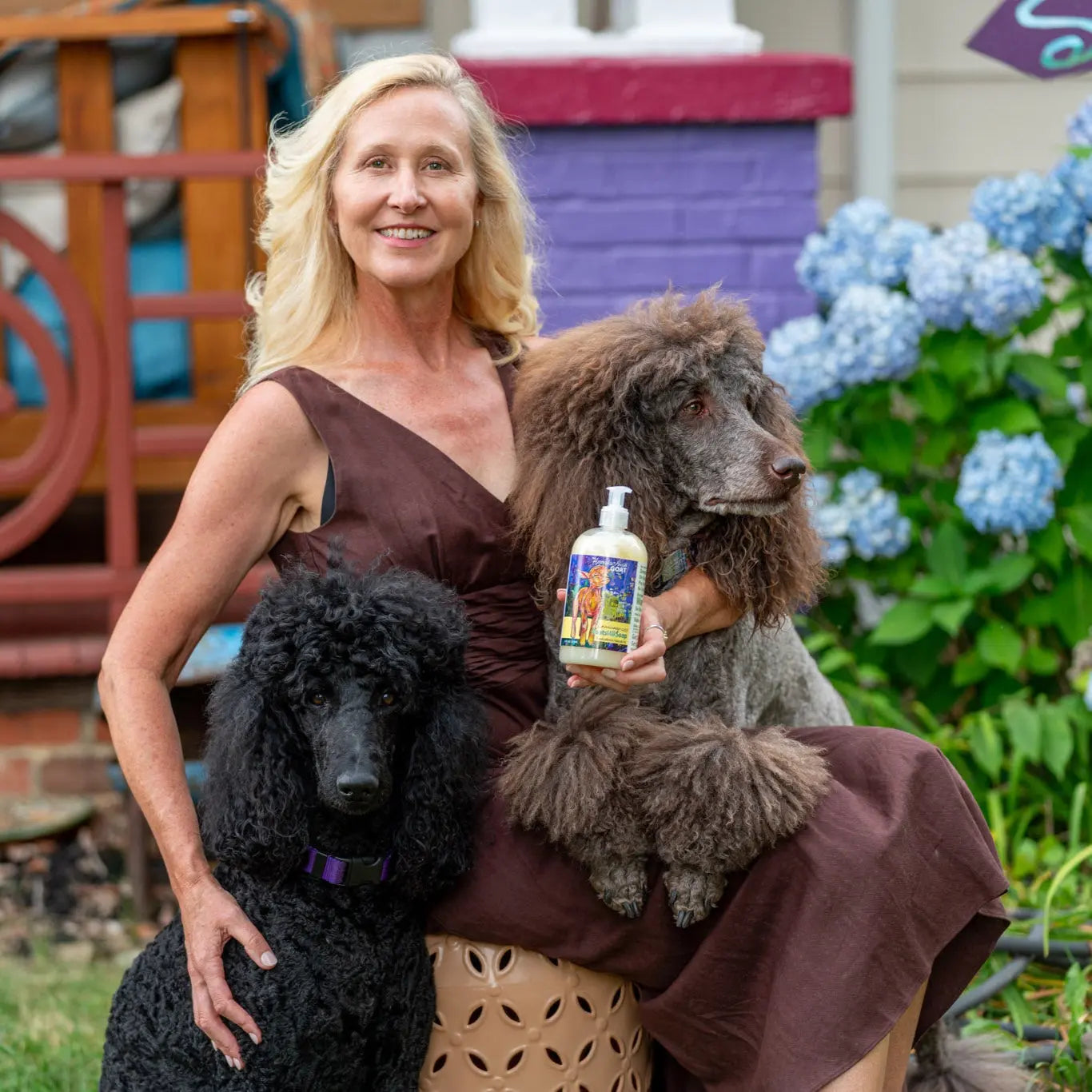Woman holding lemongrass goats milk liquid soap with two poodles
