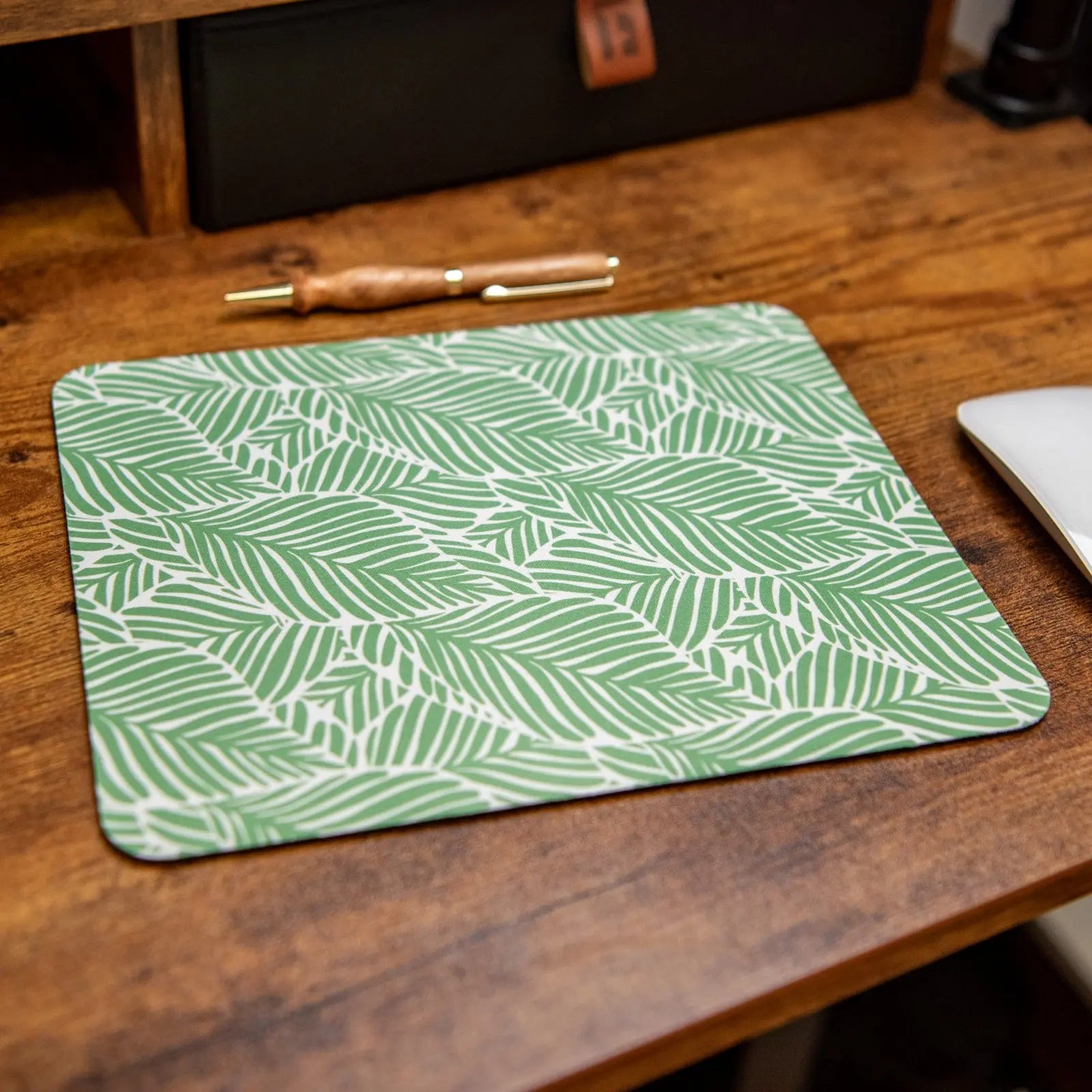 Green and white leafy palm print mouse pad on a wooden desk.