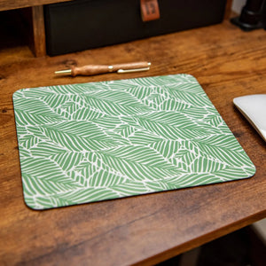 Green and white leafy palm print mouse pad on a wooden desk.