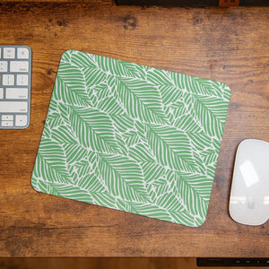 A green and white leafy pattern mouse pad on a wooden desk next to a keyboard and mouse.