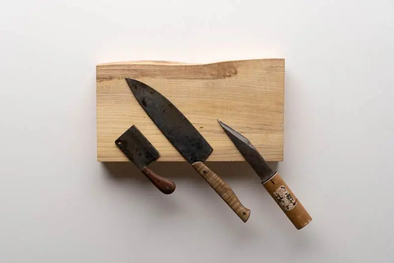 Three rustic knives (cleaver, chef, paring) displayed on a light wooden magnetic knife holder.