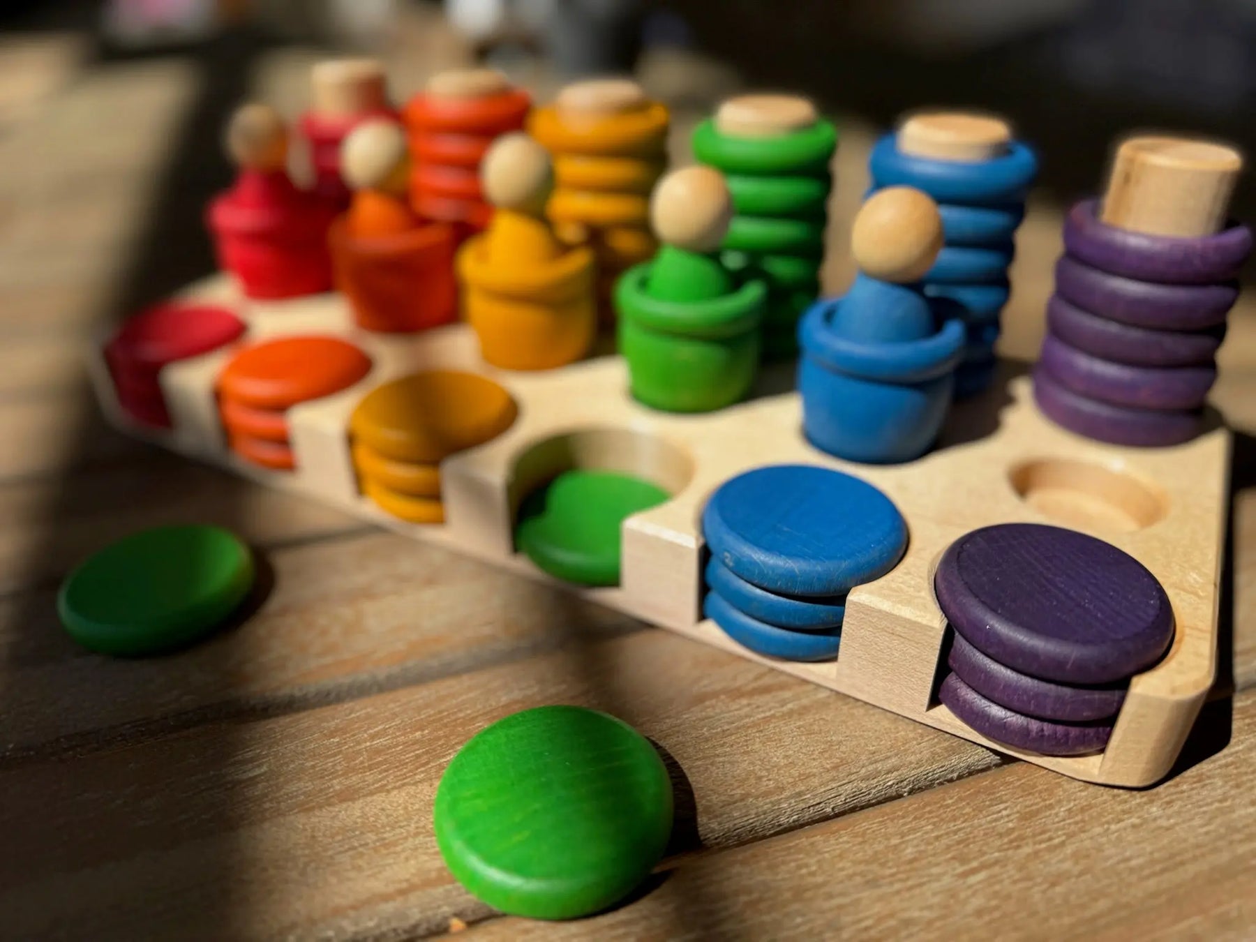 Wooden sorting tray with colorful peg figures and discs in red, orange, yellow, green, blue, and purple.
