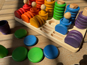 Wooden sorting tray with colored rings and figures on a wooden surface.