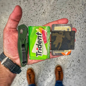 Green minimalist elastic card band wallet holding cards, cash, gum, and a knife.