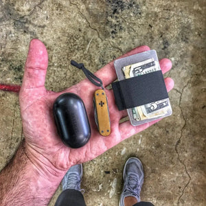 Minimalist card holder wallet with cash, Samsung earbuds, and pocket knife in hand.