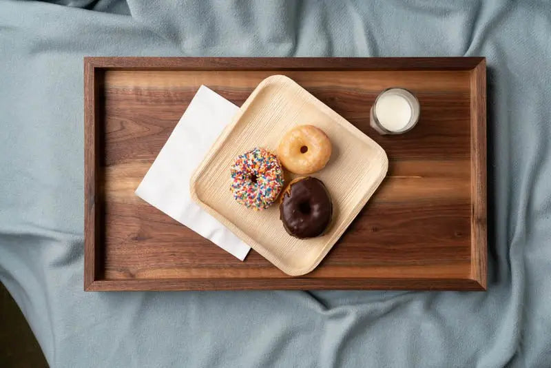 Wooden tray on a blue blanket holding a napkin, three donuts on a square plate, and a glass of milk.
