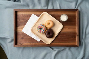 Wooden tray on a blue blanket holding a napkin, three donuts on a square plate, and a glass of milk.