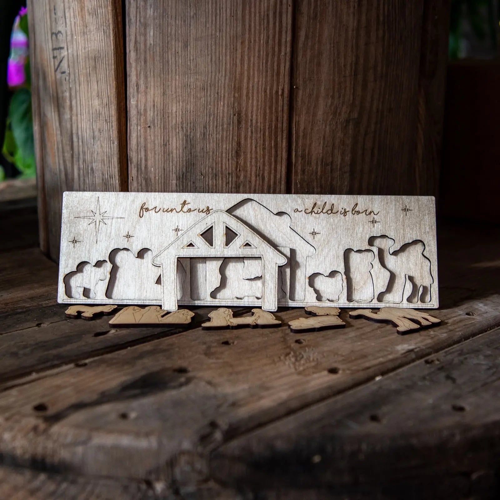 Wooden nativity puzzle with stable and scattered figures on a wood surface.