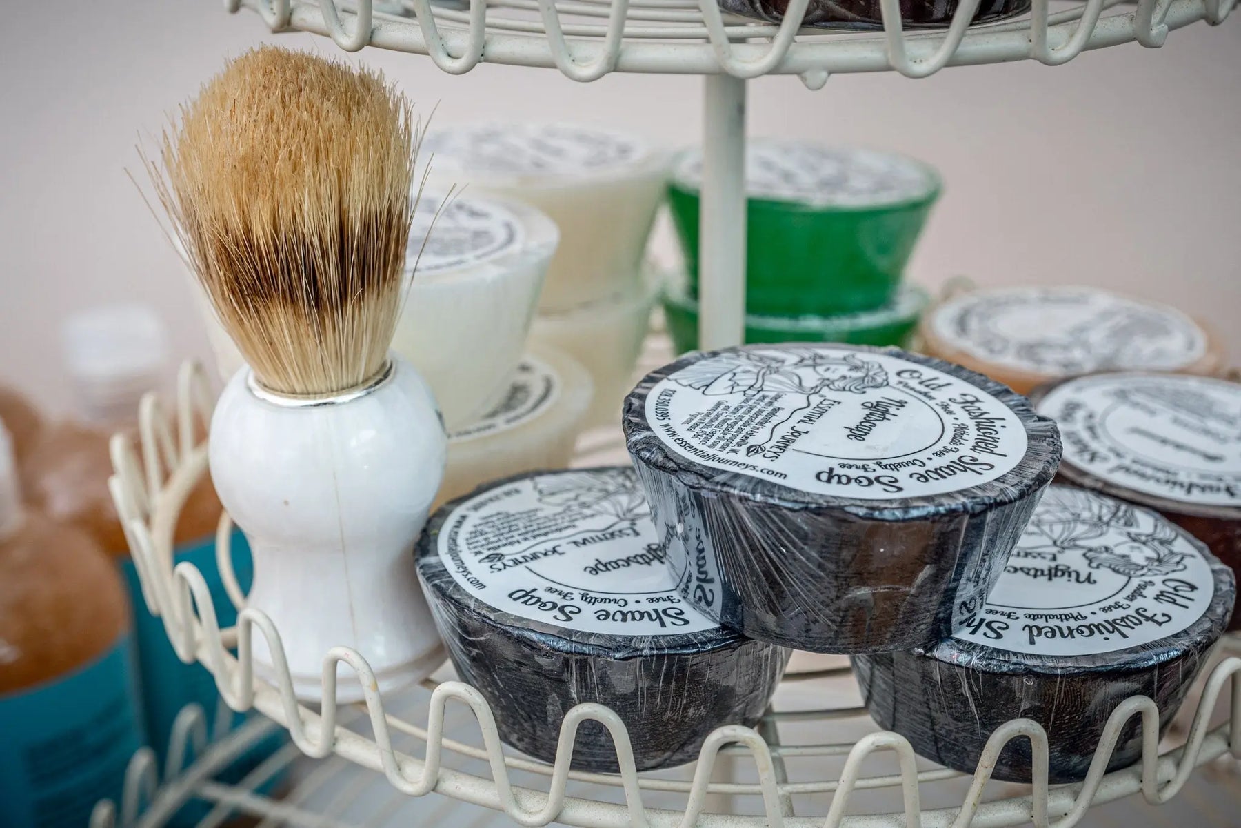 Shaving brush and Essential Journeys Old Fashioned Shave Soap bars on a white tiered stand.