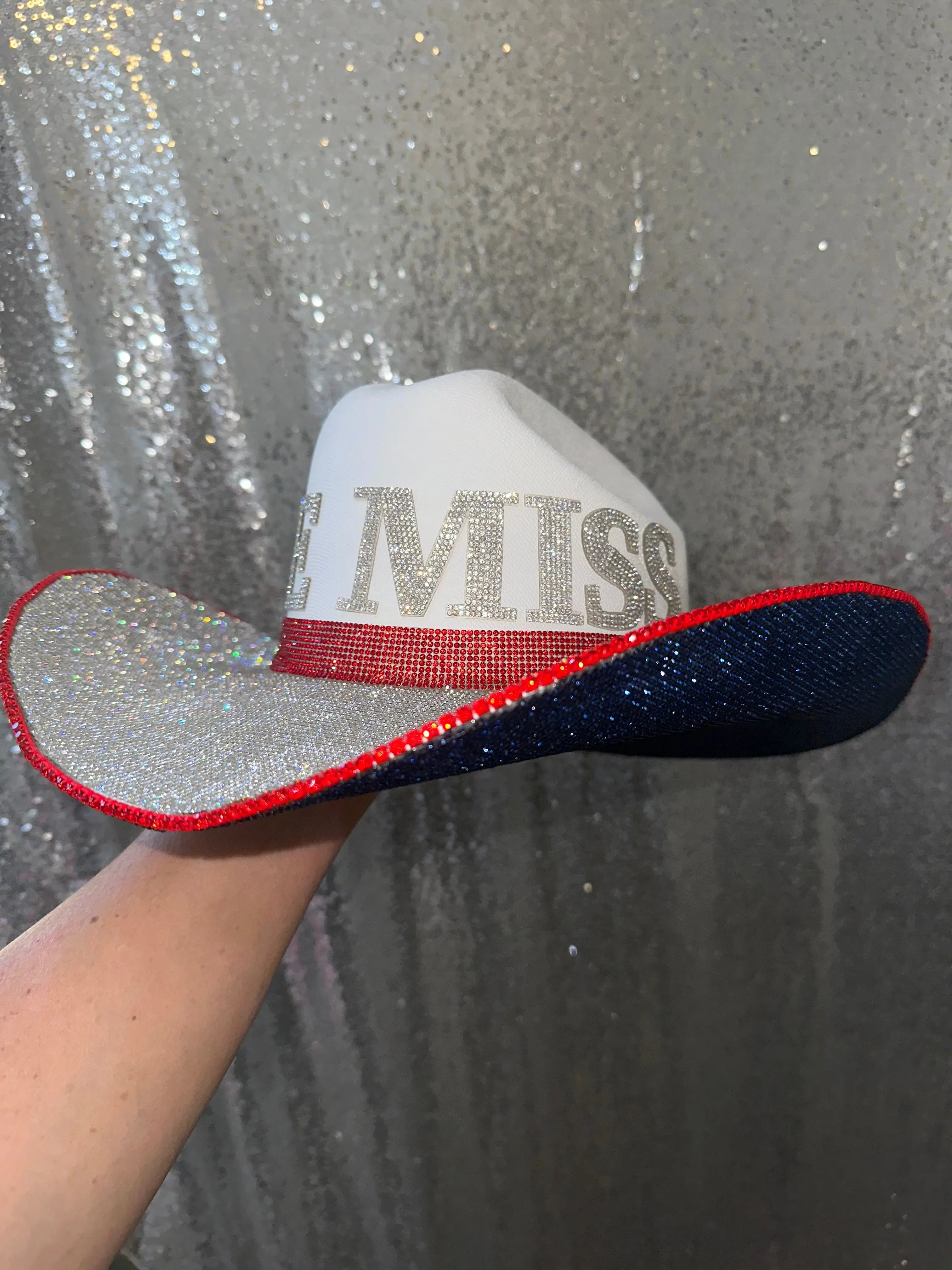White cowboy hat with "Ole Miss" rhinestone letters, red band, and sparkly brim.