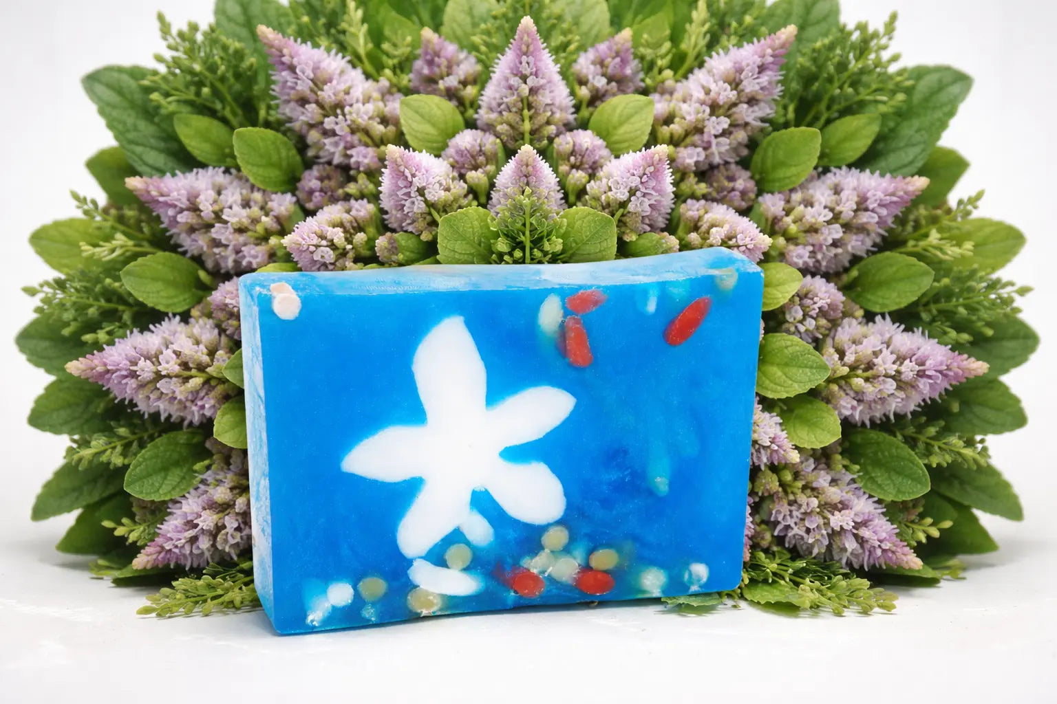 Blue soap slice with a white flower design and botanicals in a floral arrangement.