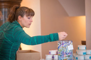 Woman putting POMEGRANATE ACAI SPF 15 LUBE FOR THE LIPS™ into a cardboard box