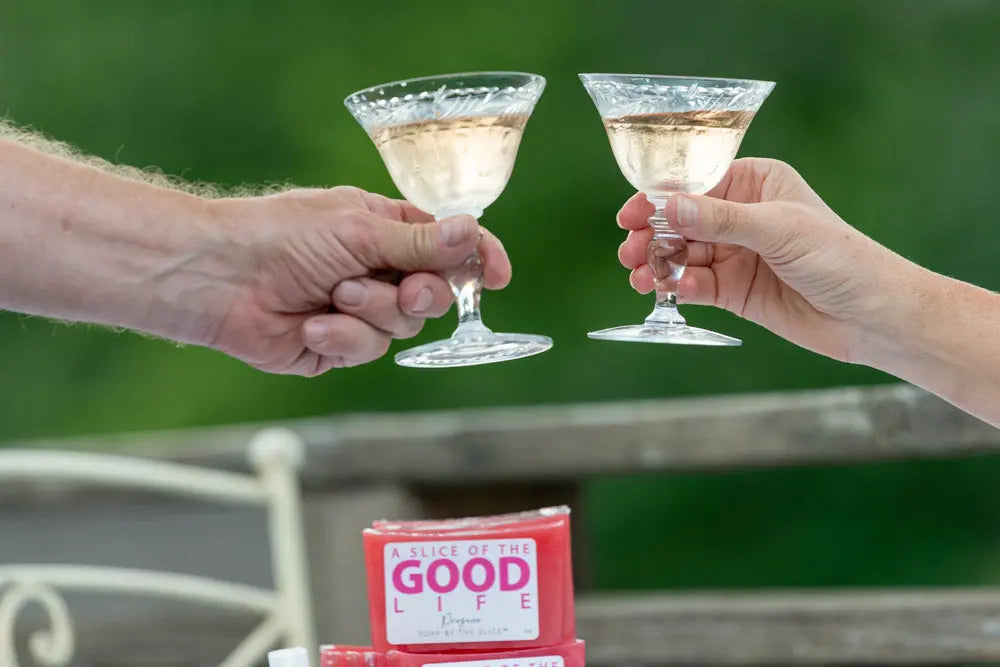 Two hands holding glasses of pink prosecco with pink soap bars in foreground.